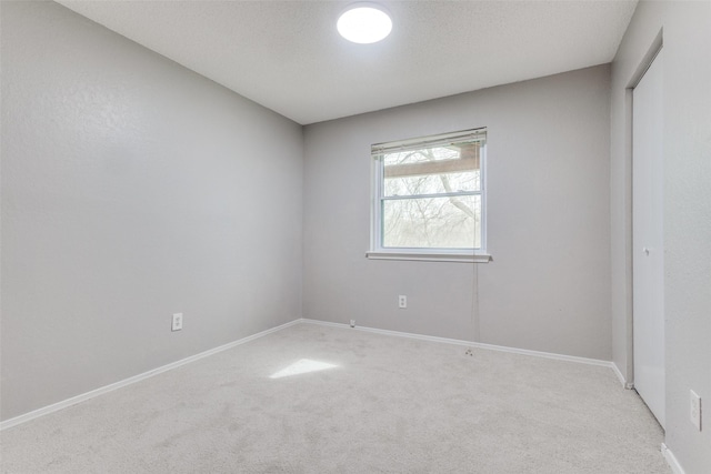 unfurnished room with light colored carpet, baseboards, and a textured ceiling