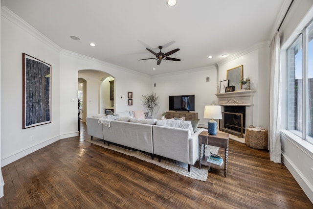 living area featuring a glass covered fireplace, dark wood finished floors, arched walkways, crown molding, and baseboards