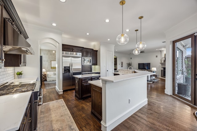 kitchen with built in appliances, dark brown cabinets, a large island with sink, and ornamental molding