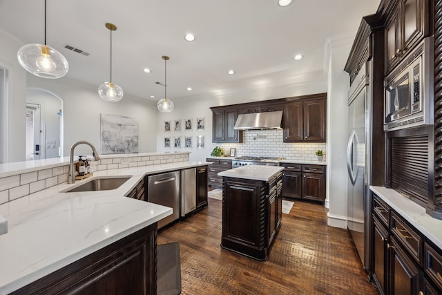 kitchen with visible vents, a sink, built in appliances, exhaust hood, and backsplash