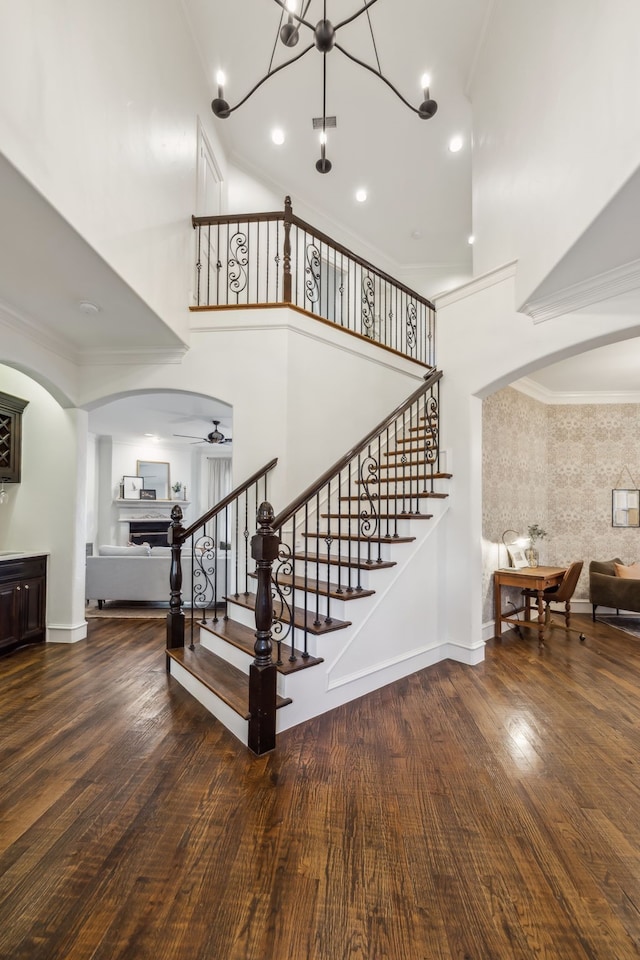 stairs featuring arched walkways, a high ceiling, wood finished floors, and crown molding