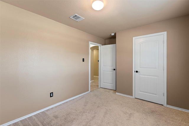 unfurnished bedroom featuring arched walkways, light colored carpet, visible vents, and baseboards