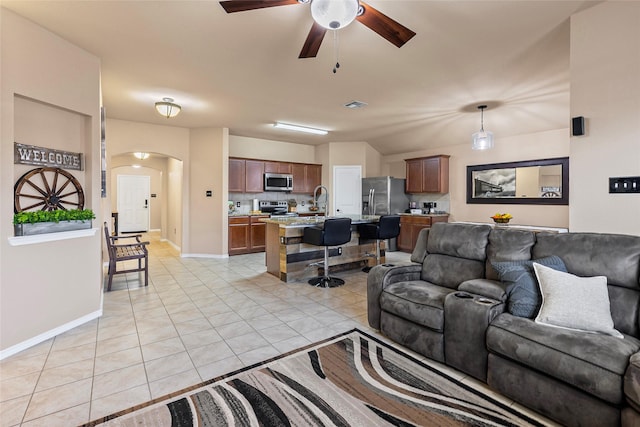 living area featuring visible vents, a ceiling fan, arched walkways, light tile patterned floors, and baseboards