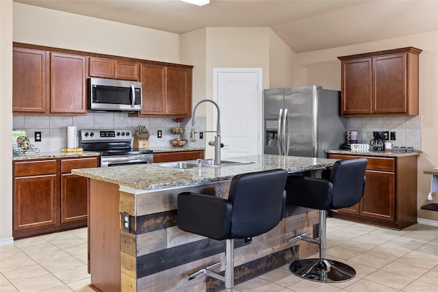 kitchen featuring light tile patterned floors, light stone counters, appliances with stainless steel finishes, and a sink