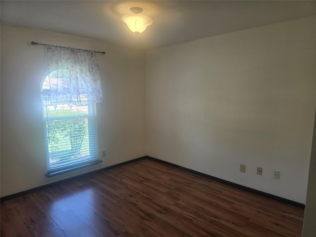 spare room with baseboards and dark wood-style floors