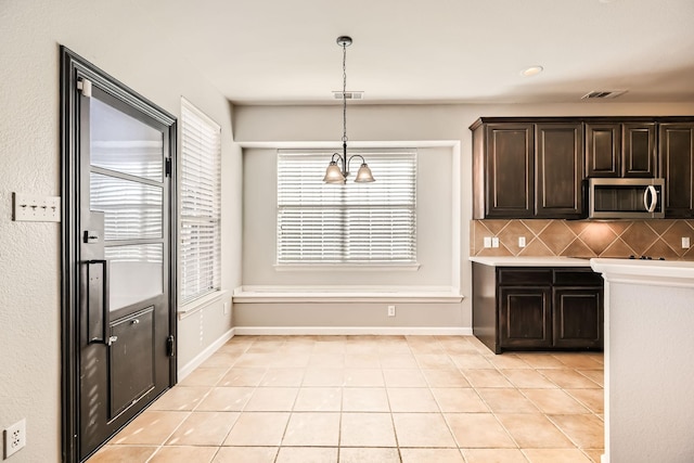 kitchen with tasteful backsplash, stainless steel microwave, dark brown cabinets, light tile patterned floors, and plenty of natural light