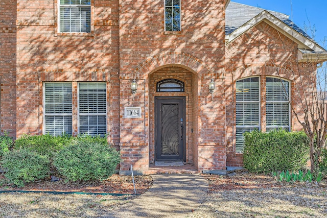 doorway to property featuring brick siding and roof with shingles