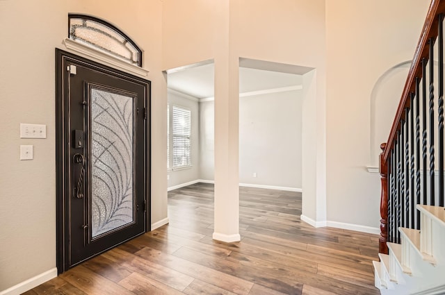 entrance foyer with baseboards, stairs, a towering ceiling, arched walkways, and wood-type flooring