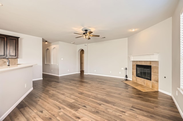 unfurnished living room featuring wood finished floors, arched walkways, ceiling fan, and a fireplace