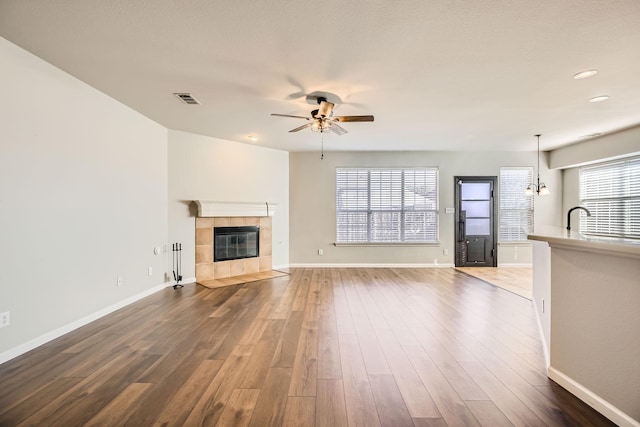 unfurnished living room featuring a tiled fireplace, wood finished floors, visible vents, and baseboards