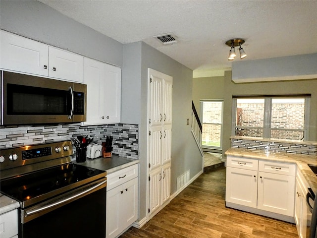 kitchen featuring visible vents, decorative backsplash, appliances with stainless steel finishes, wood finished floors, and white cabinetry