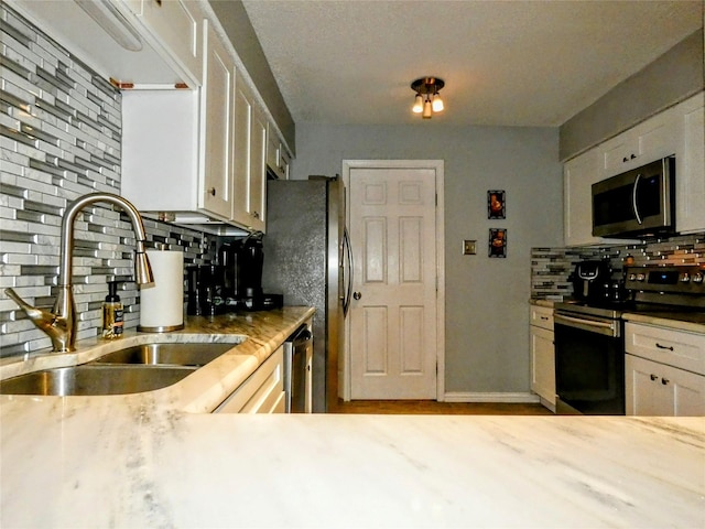 kitchen featuring light stone counters, a sink, stainless steel appliances, white cabinets, and tasteful backsplash