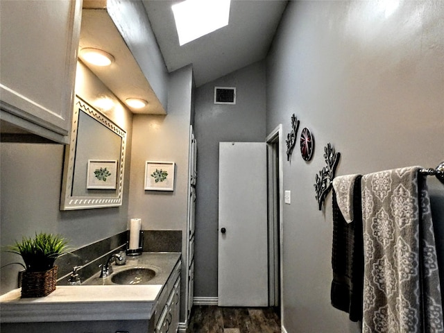 bathroom with vanity, wood finished floors, visible vents, baseboards, and vaulted ceiling