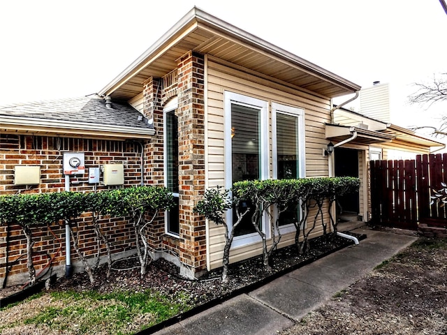 view of property exterior with brick siding, a chimney, and fence