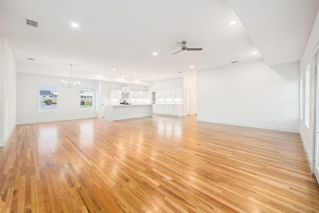 unfurnished living room featuring visible vents, baseboards, light wood-type flooring, recessed lighting, and ceiling fan with notable chandelier