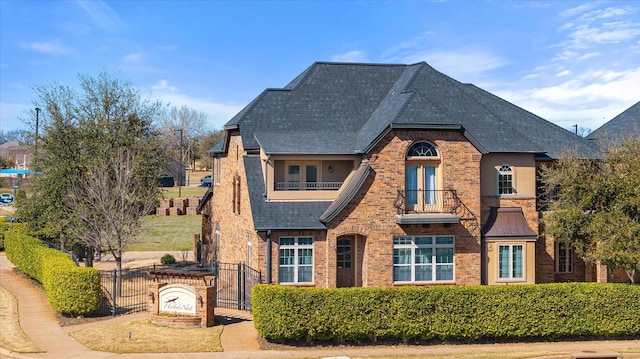 view of front of house with a balcony, a gate, stucco siding, a fenced front yard, and brick siding