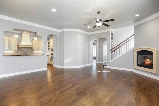 unfurnished living room with a ceiling fan, a glass covered fireplace, crown molding, baseboards, and dark wood-style flooring