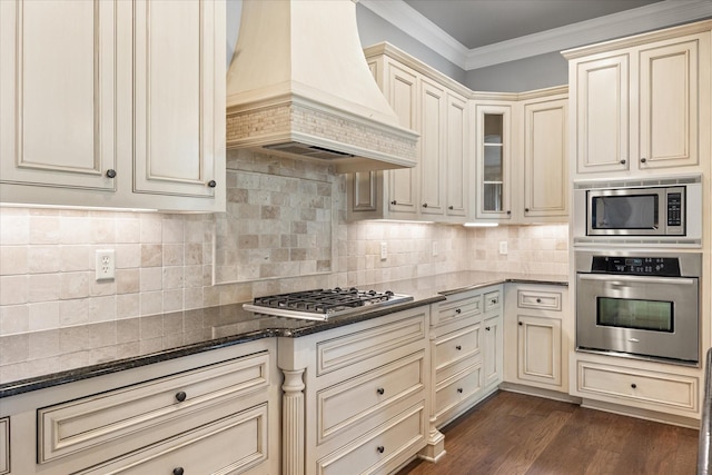 kitchen featuring custom exhaust hood, ornamental molding, dark wood-type flooring, appliances with stainless steel finishes, and cream cabinets