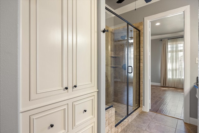 full bathroom with tile patterned floors, ornamental molding, a shower stall, baseboards, and ceiling fan