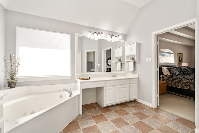 ensuite bathroom featuring vanity, a tub with jets, baseboards, lofted ceiling, and ensuite bathroom