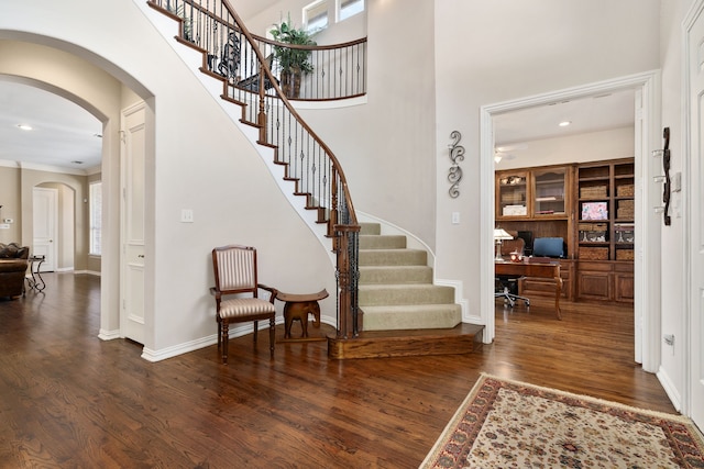 foyer entrance featuring wood finished floors, recessed lighting, arched walkways, baseboards, and a towering ceiling