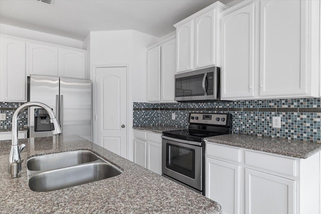 kitchen with dark stone counters, decorative backsplash, appliances with stainless steel finishes, white cabinetry, and a sink