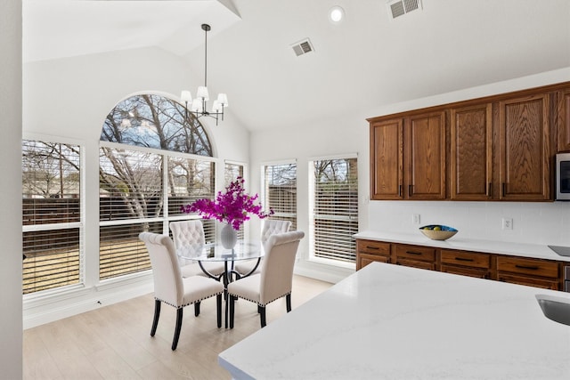 dining space with an inviting chandelier, light wood-style floors, visible vents, and high vaulted ceiling