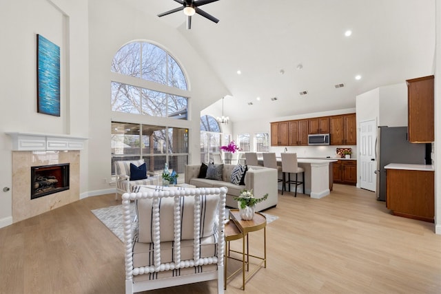 living room featuring light wood-type flooring, high vaulted ceiling, a ceiling fan, and a tile fireplace