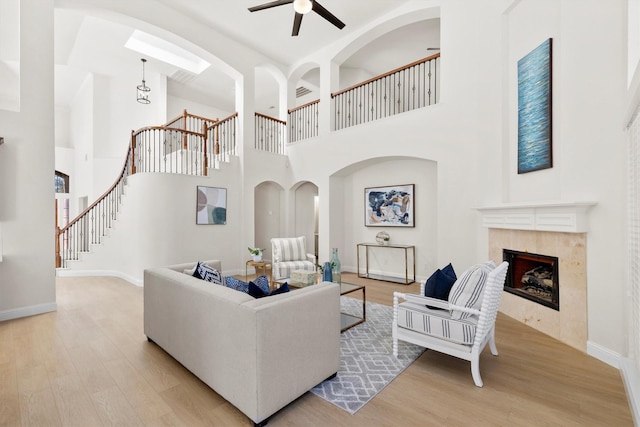 living area featuring light wood-type flooring, ceiling fan, a tiled fireplace, and stairway