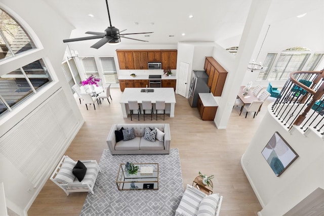 living room with baseboards, ceiling fan with notable chandelier, recessed lighting, light wood-style floors, and a towering ceiling