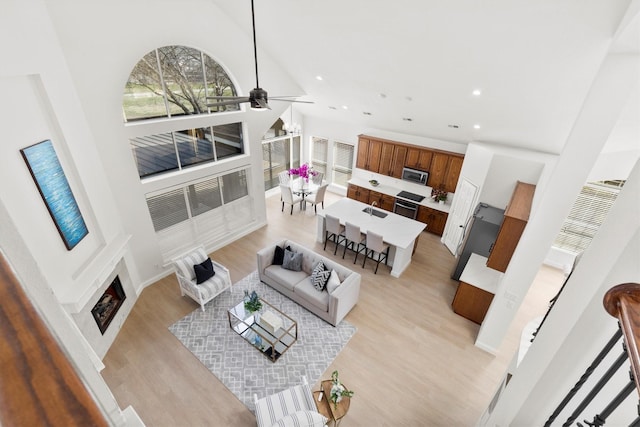 living area featuring recessed lighting, a fireplace, a high ceiling, and light wood-style floors