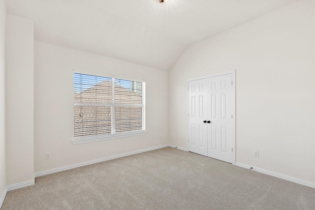 unfurnished bedroom with baseboards, lofted ceiling, light colored carpet, and a closet