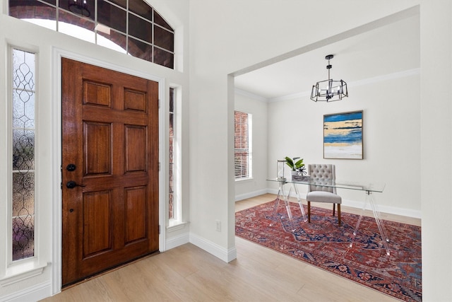 entrance foyer with baseboards, an inviting chandelier, wood finished floors, and crown molding