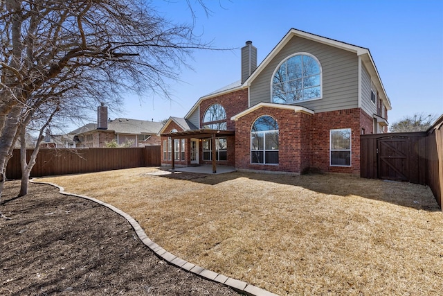 rear view of property with brick siding, a chimney, a fenced backyard, a patio, and a gate