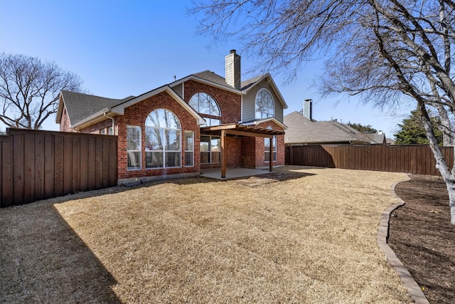 back of property featuring a patio, a fenced backyard, brick siding, and a chimney