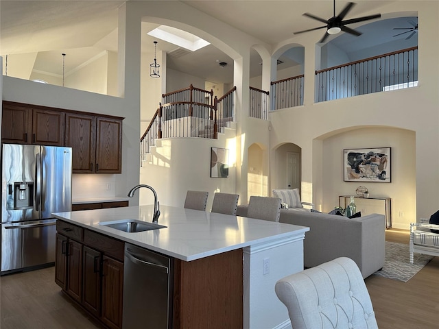 kitchen featuring a center island with sink, a sink, open floor plan, stainless steel appliances, and light countertops