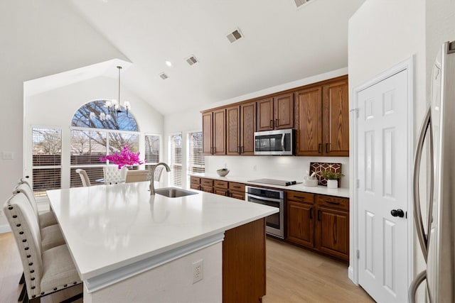 kitchen with visible vents, a sink, lofted ceiling, appliances with stainless steel finishes, and a kitchen island with sink