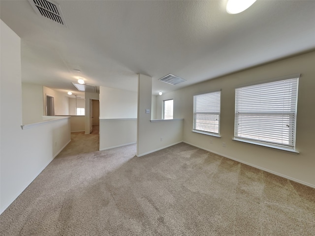 carpeted empty room with visible vents, baseboards, and attic access