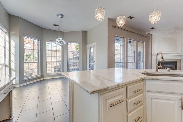 kitchen featuring a sink, visible vents, light stone counters, and a glass covered fireplace