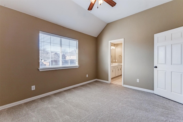 unfurnished bedroom featuring baseboards, light colored carpet, lofted ceiling, ensuite bathroom, and a ceiling fan