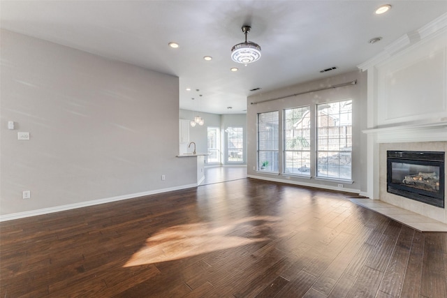 unfurnished living room with dark wood-style floors, visible vents, baseboards, recessed lighting, and a tile fireplace