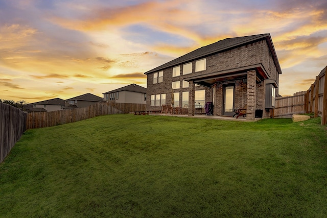 rear view of house with a patio, a lawn, brick siding, and a fenced backyard