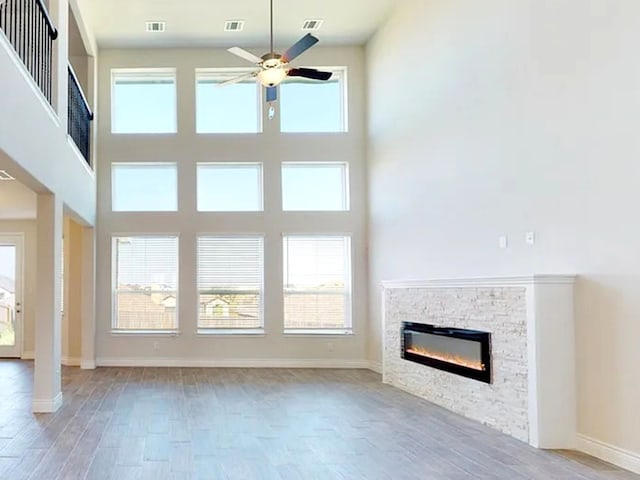 unfurnished living room with a stone fireplace, wood finished floors, baseboards, and ceiling fan