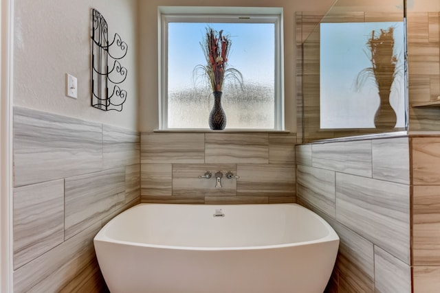 full bath featuring a soaking tub and tile walls