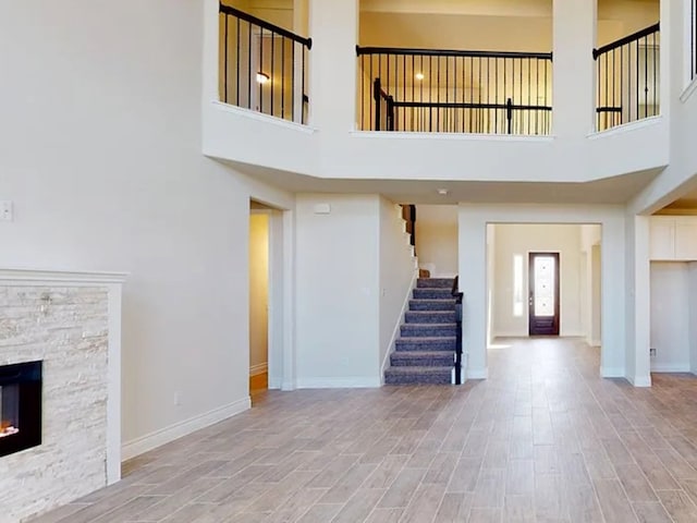 unfurnished living room with a stone fireplace, stairway, baseboards, and wood finished floors