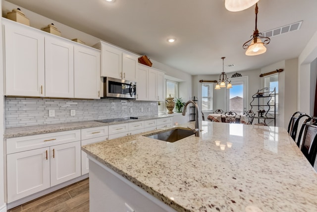 kitchen featuring visible vents, a sink, white cabinets, stainless steel microwave, and backsplash