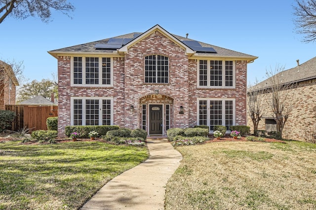 view of front facade featuring roof mounted solar panels, brick siding, and a front yard