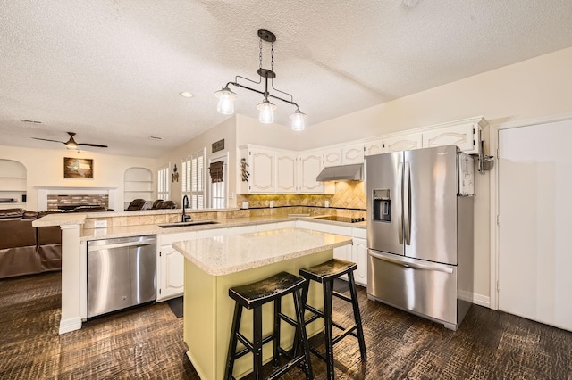 kitchen featuring under cabinet range hood, open floor plan, stainless steel appliances, white cabinetry, and a sink