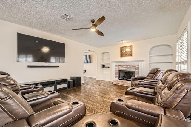 living area with visible vents, built in features, a textured ceiling, wood finished floors, and a brick fireplace