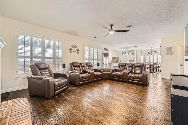 living area with visible vents, ceiling fan with notable chandelier, baseboards, and a textured ceiling